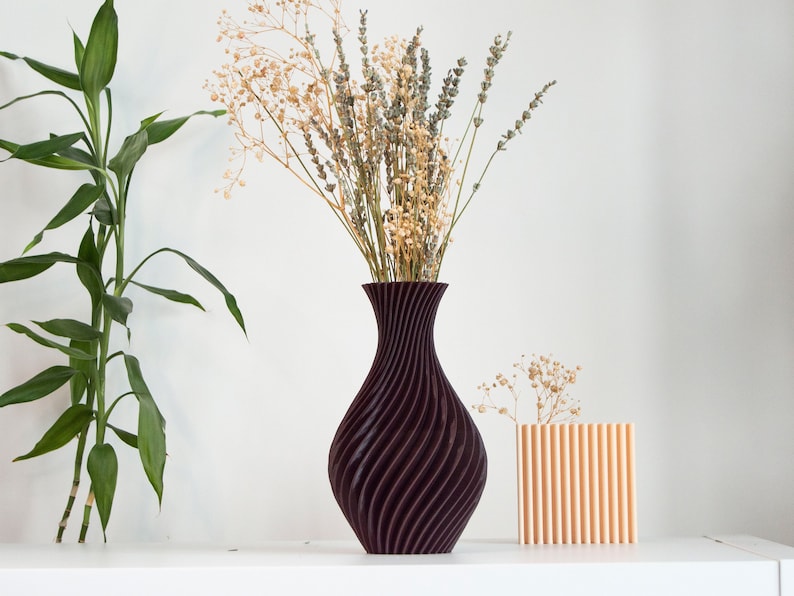 Pu&ograve; includere: Due vasi con fiori secchi. Il vaso pi&ugrave; grande &egrave; di colore viola scuro con un motivo a spirale. Il vaso pi&ugrave; piccolo &egrave; di colore arancione chiaro con un motivo a coste verticali.