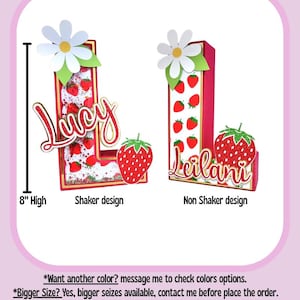 May include: Two 8-inch tall letters, "L" and "L", decorated with a strawberry and daisy theme. The "L" on the left is a shaker design with glitter inside. The "L" on the right is a non-shaker design. Both letters have the names "Lucy" and "Leilani" written on them.