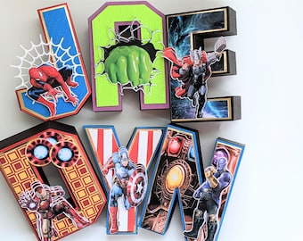 Op de afbeelding: Een set van zes kleurrijke kartonnen letters die de naam "JADEYN" spellen, versierd met verschillende Marvel-superheldenfiguren. De letters zijn versierd met afbeeldingen van Spider-Man, Hulk, Thor, Iron Man, Captain America en Thanos.