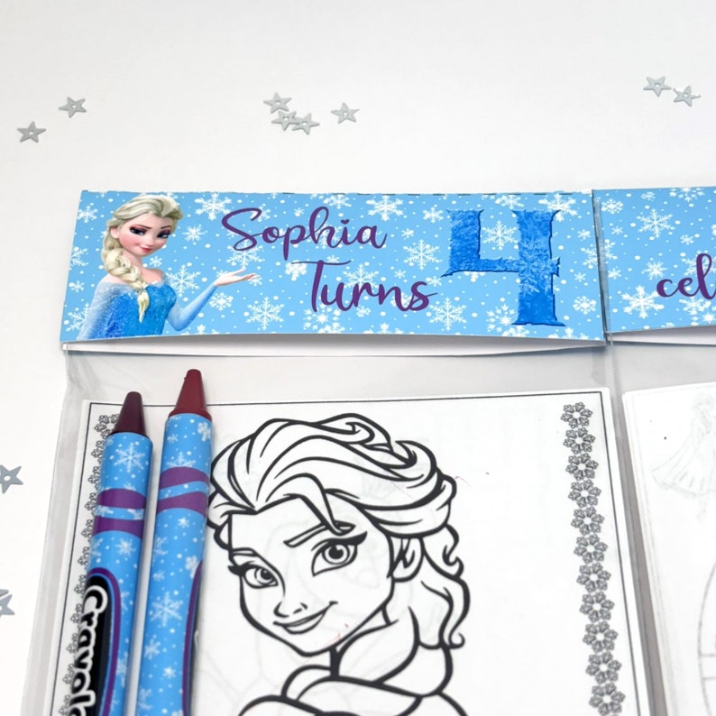 May include: A blue and white party favour bag with a Frozen-themed colouring page featuring Elsa. The bag includes two crayons, one red and one blue. The bag has a label that says "Sophia Turns 4".