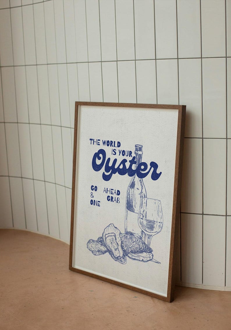 May include: Framed print with a blue illustration of oysters, a wine bottle, and a glass. The text "THE WORLD IS YOUR OYSTER" is displayed in blue, along with "GO AHEAD & GRAB ONE". The frame is brown.