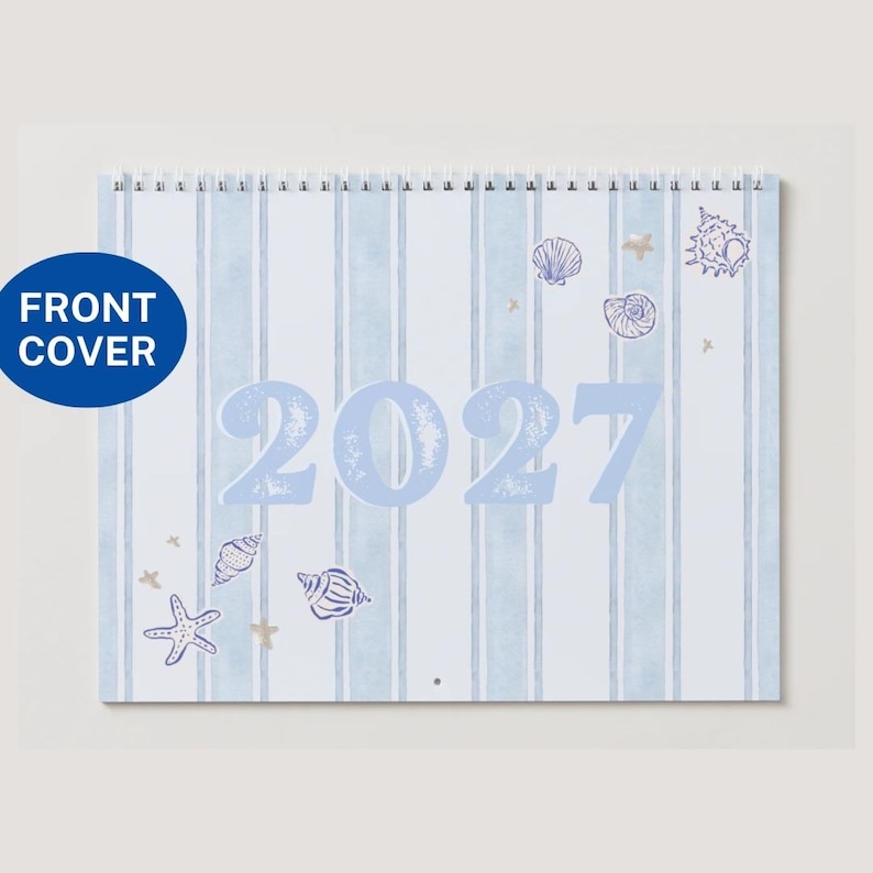 May include: A spiral-bound wall calendar with a light blue and white vertical striped background. The front cover features the year 2027 in large light blue numbers, decorated with illustrations of various seashells and starfish in blue and tan.