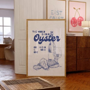 May include: A framed print with the text "THE WORLD IS YOUR Oyster" in blue script, accompanied by a bottle, glass, and oysters illustration. The print is in a room with other framed art and wooden furniture.