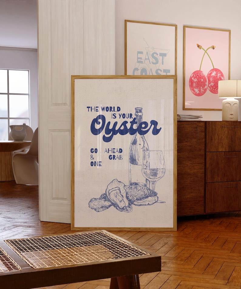 May include: A framed print with the text "THE WORLD IS YOUR Oyster" in blue script, accompanied by a bottle, glass, and oysters illustration. The print is in a room with other framed art and wooden furniture.