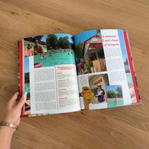 Op de afbeelding: Een open boek met een reisgids-indeling met meerdere kleurenfoto's van een zwembad, een burgerrestaurant en mensen die van zomeractiviteiten genieten. De pagina's bevatten gedrukte tekst en rode koppen over lokale zomerse rituelen.