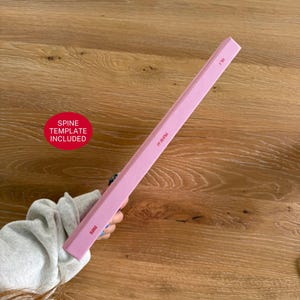 Pu&ograve; includere: Un dorso di libro rosa chiaro con testo rosso che recita 2025 e include un grafico circolare rosso con il testo bianco SPINE TEMPLATE INCLUDED. Il dorso &egrave; rettangolare e di colore solido, mostrando chiari dettagli di branding per un'agenda.