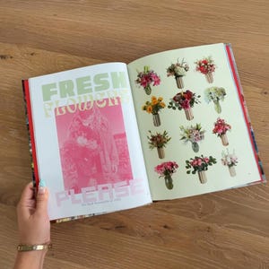 Op de afbeelding: Een open boek met een pagina met de tekst FRESH FLOWERS PLEASE in grote groene en roze letters over een roze getinte foto van een persoon die bloemen vasthoudt. De tegenoverliggende pagina toont een raster van twaalf kleine boeketten.