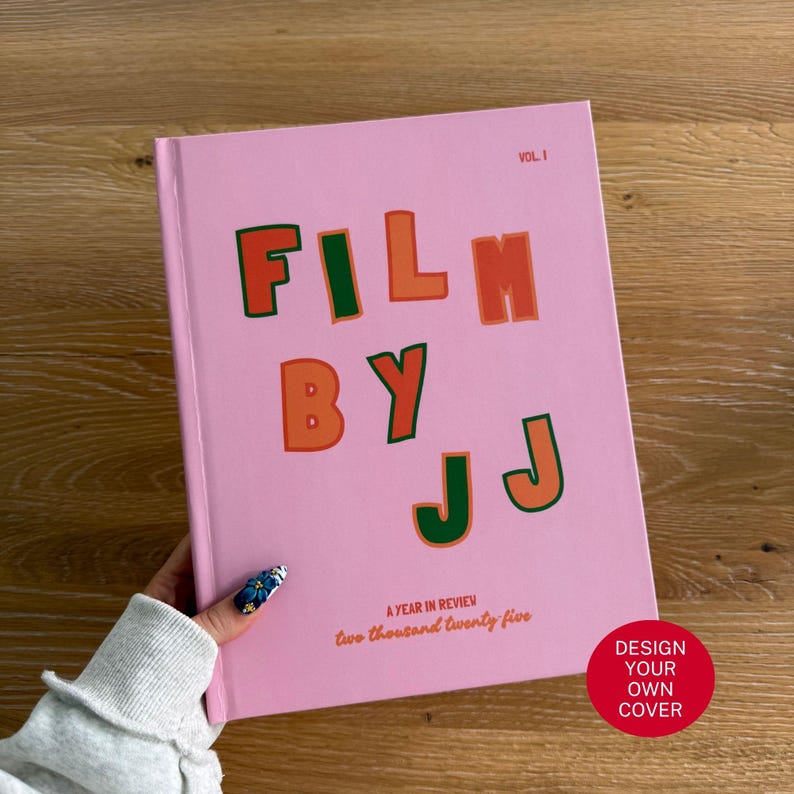 Pu&ograve; includere: Un libro con copertina rigida rosa con il testo FILM BY JJ VOL. I e A YEAR IN REVIEW two thousand twenty five stampato sulla copertina in lettere verdi e arancioni. Il libro ha una finitura opaca liscia e una forma rettangolare.