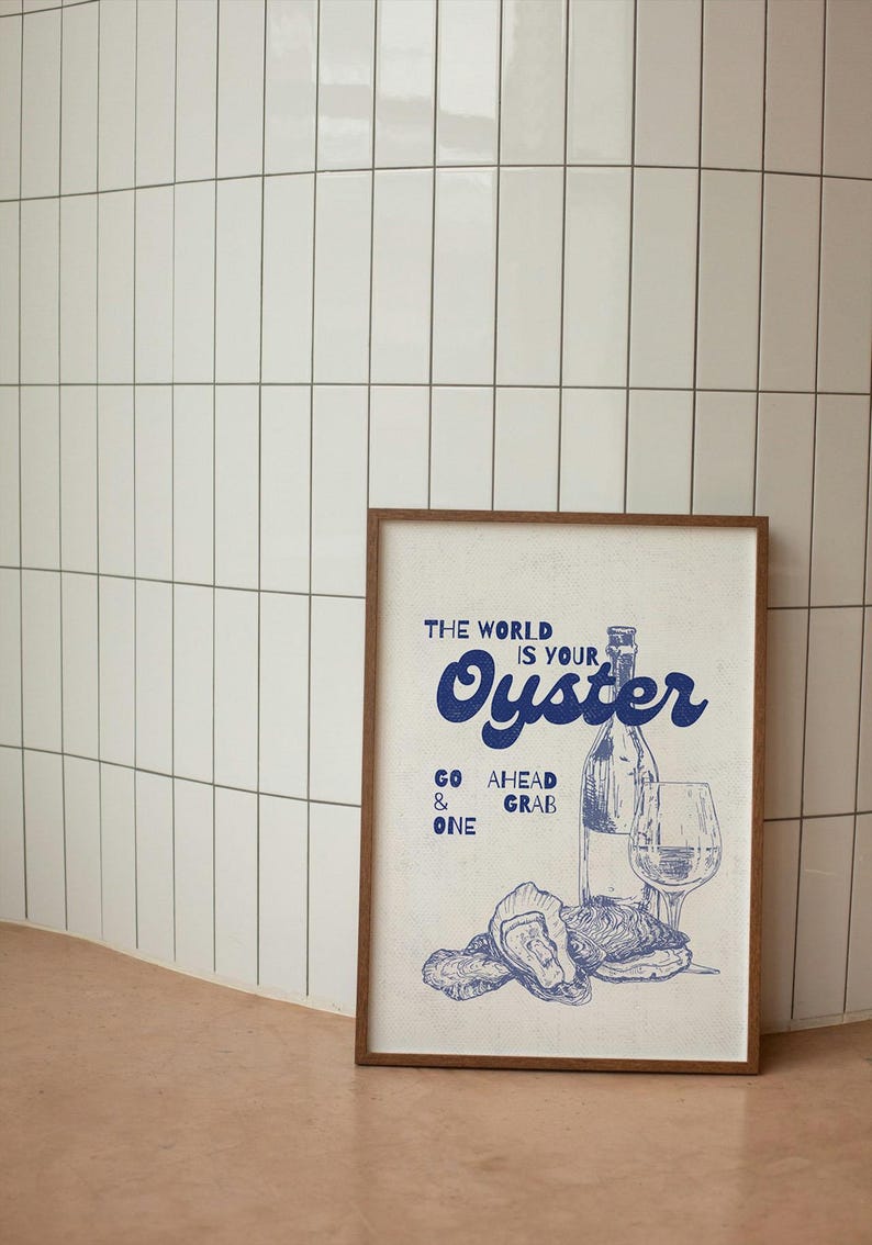 May include: A framed print with a vintage-style illustration in blue. The artwork features a wine bottle, a wine glass, and oysters, with the text "THE WORLD IS YOUR OYSTER." The phrase "GO AHEAD & GRAB ONE" is also included.