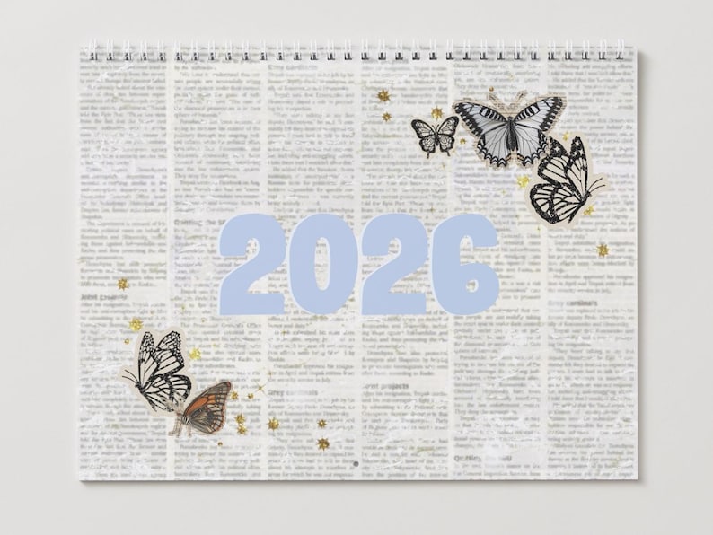 May include: A spiral-bound calendar with a newspaper print background. The light blue numbers "2026" are centered. Butterflies in black, white, and brown are scattered across the page, along with gold star accents. A decorative calendar.