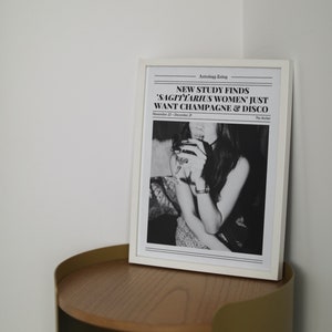 May include: A black and white framed print with the text "NEW STUDY FINDS 'SAGITTARIUS WOMEN' JUST WANT CHAMPAGNE & DISCO" and the date "November 22 - December 20". The print features a black and white photo of a woman holding a glass of wine.