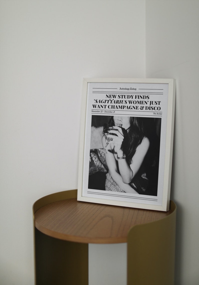 May include: A black and white framed print with the text "NEW STUDY FINDS 'SAGITTARIUS WOMEN' JUST WANT CHAMPAGNE & DISCO" and the date "November 22 - December 20". The print features a black and white photo of a woman holding a glass of wine.