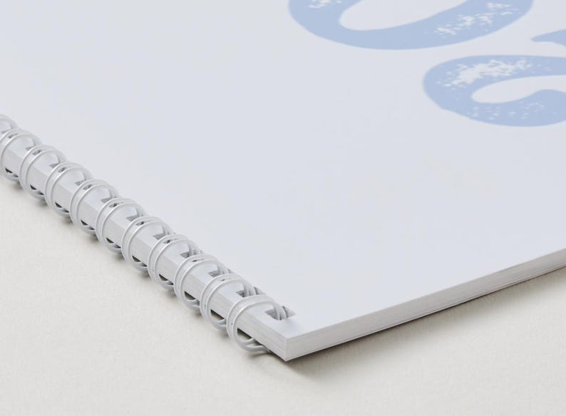 May include: A white spiral-bound notebook featuring a light blue graphic design on the cover. The binding consists of a white plastic coil that holds the pages together along the left edge. The cover displays a partial light blue number 202.