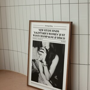 May include: A framed black and white photo of a woman holding a glass of champagne. The photo has a newspaper headline that reads "NEW STUDY FINDS 'SAGITTARIUS WOMEN' JUST WANT CHAMPAGNE & DISCO" with the text "Astrology Today" and "The Archer" at the top and bottom of the headline.