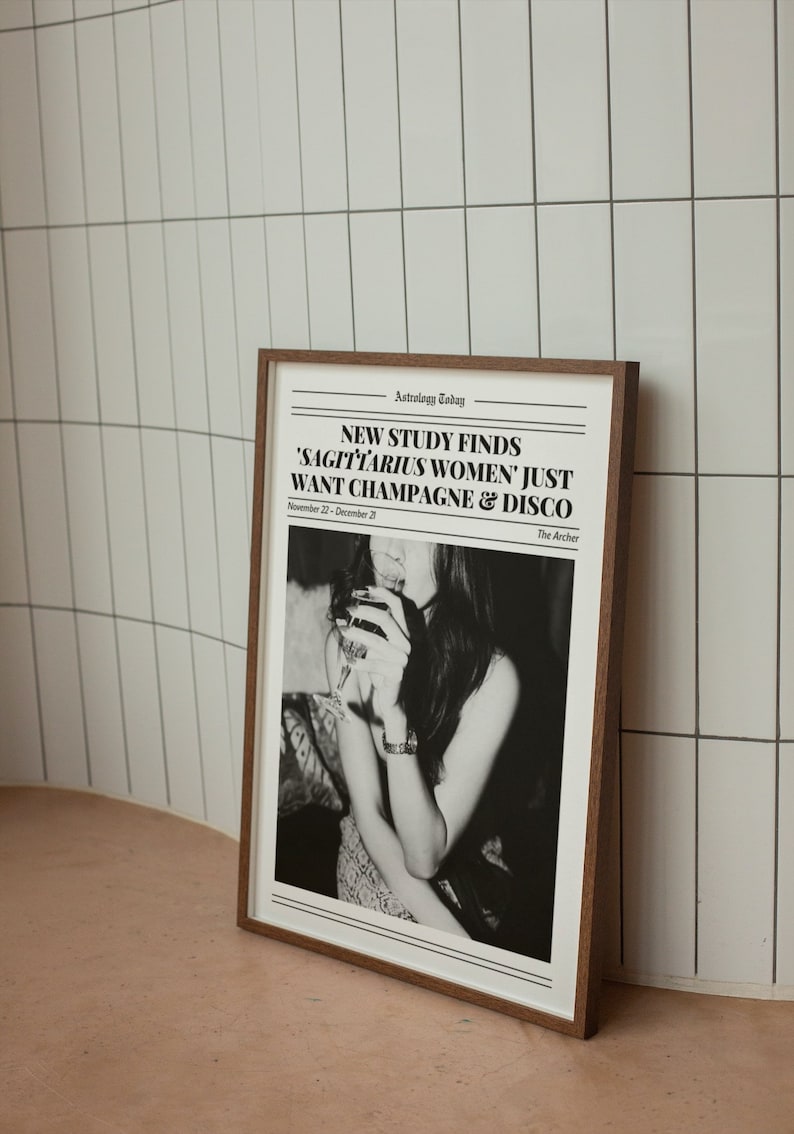 May include: A framed black and white photo of a woman holding a glass of champagne. The photo has a newspaper headline that reads "NEW STUDY FINDS 'SAGITTARIUS WOMEN' JUST WANT CHAMPAGNE & DISCO" with the text "Astrology Today" and "The Archer" at the top and bottom of the headline.