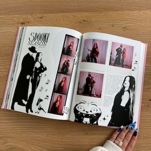 Pu&ograve; includere: Un libro aperto che mostra una pagina intitolata SPOOKY SEASON con illustrazioni in bianco e nero di due figure, note musicali e un muso di gatto. La pagina include una striscia verticale di quattro foto e due foto quadrate in stile polaroid.