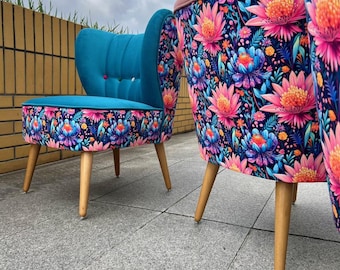 May include: Two accent chairs featuring a vibrant floral pattern with pink and blue lotus-like flowers on a dark background. The chairs have light-colored wooden legs, a teal velvet interior, and a pink velvet top edge on the backrest.