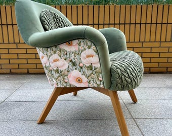 May include: An armchair featuring sage green velvet upholstery with a ruched texture on the seat and backrest. The exterior side panel displays a floral pattern with light pink poppies and white flowers on a light background, supported by four light wood legs.
