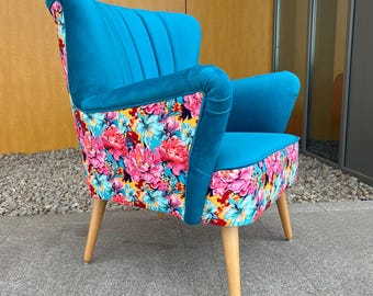 May include: An armchair featuring a vibrant turquoise velvet upholstery on the inner back, seat, and arms, contrasted with a colorful floral print fabric on the outer back and base. The chair is supported by four light-colored wooden legs.
