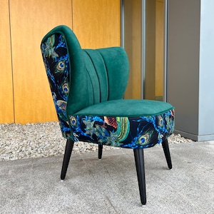 May include: A teal accent chair with a curved back and black legs. The back and seat trim feature a peacock feather pattern on a black background, while the backrest is a solid teal color. The chair is designed for indoor use.