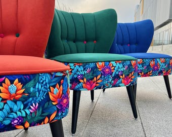 May include: Three chairs with black tapered legs and tufted backrests in red, green, and blue. The seat bases feature a vibrant floral pattern with orange, pink, and blue leaves and flowers. The backrests include small, contrasting circular buttons.