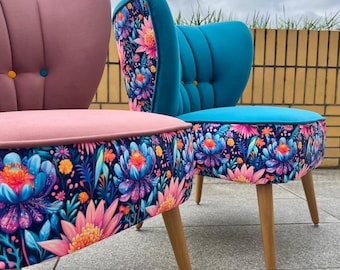 May include: Two upholstered chairs with light wood legs. One chair is dusty pink with a button-tufted back and a dark blue base featuring a vibrant floral pattern. The other chair is teal with a button-tufted back and a matching floral base.