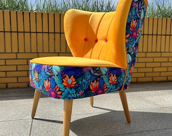 May include: An accent chair featuring a vibrant mustard yellow velvet interior with vertical channel tufting and three small pink buttons. The exterior and seat base are upholstered in a colorful fabric with a dense tropical floral pattern.