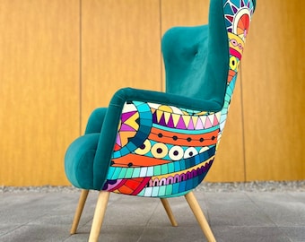 May include: A wingback chair featuring solid teal velvet upholstery on the front and sides, contrasted by a vibrant, multi-colored geometric pattern on the back. The chair is supported by four light-toned wooden legs angled outward for stability.