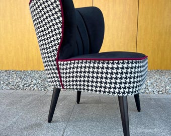 Puede incluir: Una silla decorativa con patrón de pata de gallo en blanco y negro en el exterior y la base del asiento, contrastada con tapicería de terciopelo negro sólido en el respaldo interior. La silla incluye ribetes de color rojo oscuro y cuatro patas negras cónicas.