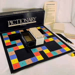 May include: A complete Pictionary board game set. The black game board is open, revealing colorful squares and the game's path. Includes a box, cards, pencils, dice, and a timer. The box reads "PICTIONARY THE GAME OF QUICK DRAW FIRST EDITION."