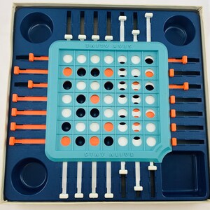 Pode incluir: Um jogo de tabuleiro vintage, "Stay Alive", numa caixa azul e branca. O tabuleiro &eacute; turquesa com pe&ccedil;as de jogo laranja, pretas e brancas. O t&iacute;tulo do jogo est&aacute; impresso no tabuleiro. O jogo inclui controles deslizantes e pinos.