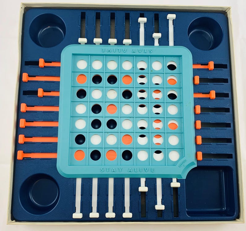 Pode incluir: Um jogo de tabuleiro vintage, "Stay Alive", numa caixa azul e branca. O tabuleiro &eacute; turquesa com pe&ccedil;as de jogo laranja, pretas e brancas. O t&iacute;tulo do jogo est&aacute; impresso no tabuleiro. O jogo inclui controles deslizantes e pinos.