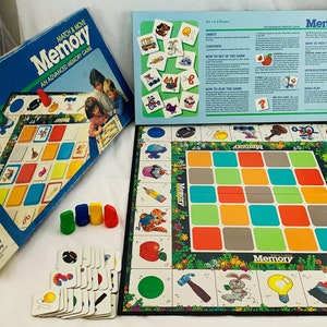 May include: A vintage "Memory" board game by MB. The box is blue with the game title and children's illustrations. The game includes a game board, cards, and colored game pieces. The game board has a grid of colorful squares.