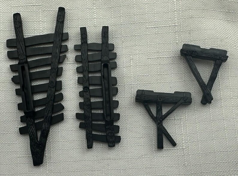 May include: Four black miniature wooden structures, including two fences and two tables. The fences have horizontal slats and vertical supports. The tables have a triangular or rectangular top with angled legs. The items are likely for a model or diorama.