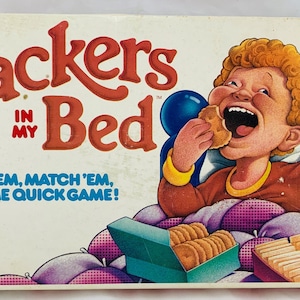 May include: Vintage "Crackers in My Bed" board game box. The box features a cartoon illustration of a child eating crackers in bed. The game's title is in large red letters, with the text "FIND 'EM, MATCH 'EM, FEED ME QUICK GAME!" below. The Parker Brothers logo is in the bottom left corner.