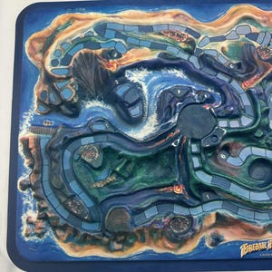 May include: A detailed board game with a coastal theme. The game board features a blue ocean, sandy beaches, and winding pathways. The board has a dark blue border and is labeled with the game's title, "Fireball Island".