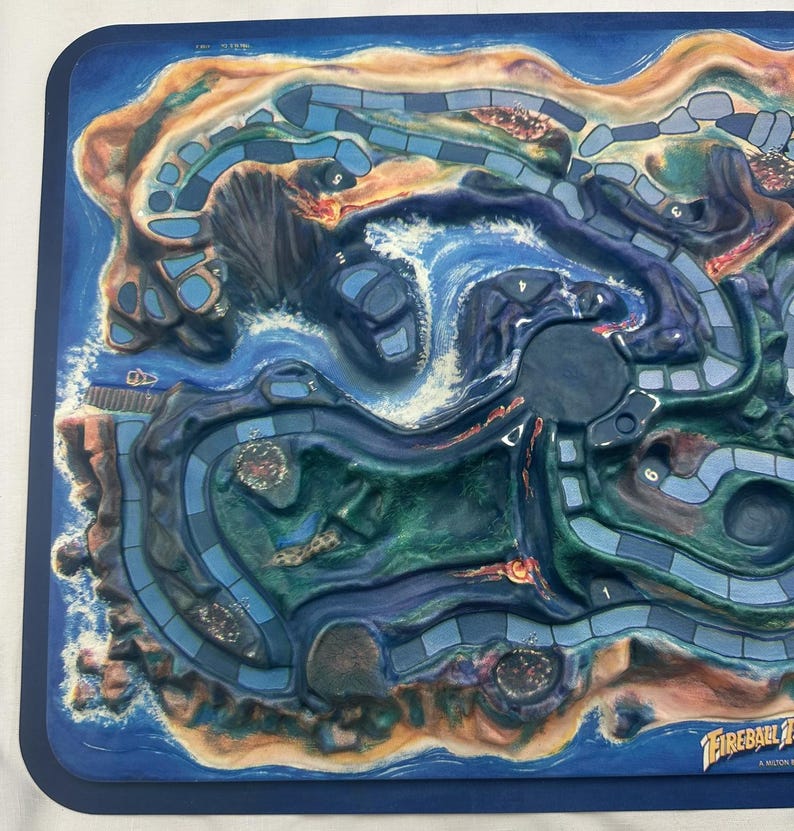 May include: A detailed board game with a coastal theme. The game board features a blue ocean, sandy beaches, and winding pathways. The board has a dark blue border and is labeled with the game's title, "Fireball Island".