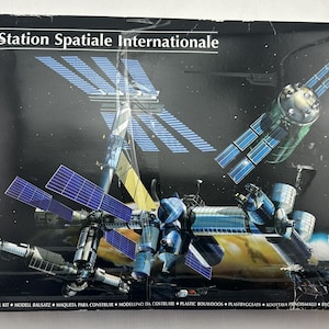 May include: A model kit box featuring a detailed illustration of the International Space Station. The box has the text "1.125 Station Spatiale Internationale" and the Heller logo. The image shows the space station with solar panels and various modules.