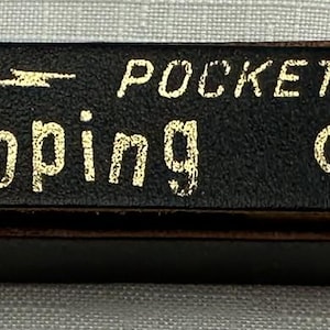May include: A black leather pocket case with gold lettering that reads "Galloping GOLF". The word "POCKET" is also in gold lettering. The case has a snap closure on the right side.