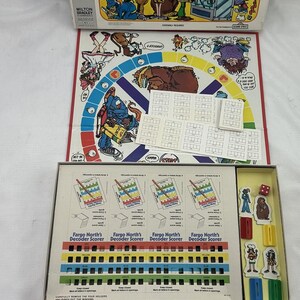 May include: The Fargo North, Decoder secret word game by Milton Bradley includes a colorful game board, a box with four decoder scorers, character standees, a red die, and various paper cards featuring cartoon illustrations and text.