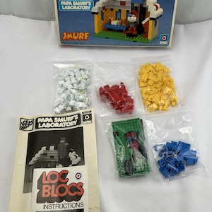 May include: A vintage Smurf's Laboratory building set from the Loc Blocs toy line. The set includes 200 pieces, a Smurf character, and instructions. The box is blue and white with the words "Loc Blocs" and "Papa Smurf's Laboratory" printed on it.