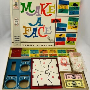 May include: A vintage board game called "Make a Face" by Milton Bradley Company. The game box is open, revealing the game board, playing pieces, and money. The game board has a red and white grid with numbers 1 through 6. The game pieces are colorful and include faces, hats, and other accessories. The money is in denominations of 50 and 100.