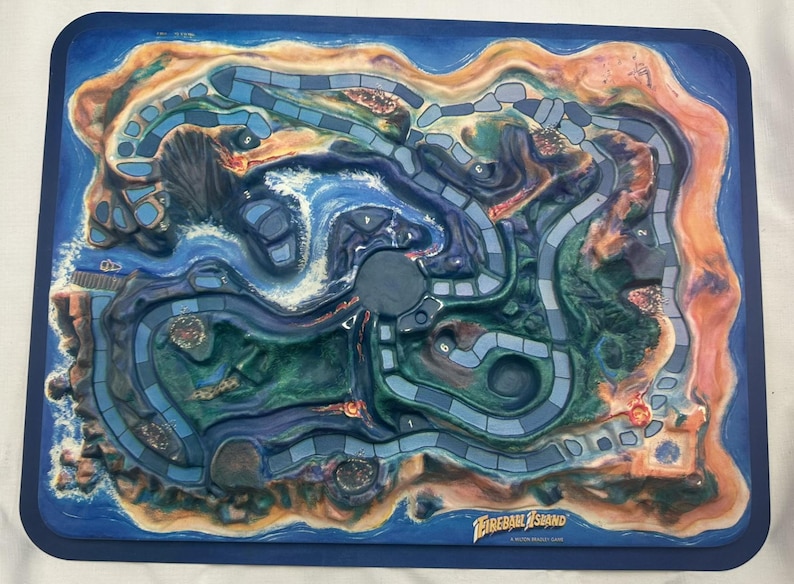 May include: A Fireball Island board game with a detailed island landscape. The game board features a blue ocean, green and brown landmasses, and a winding path. The game's title is visible in the lower right corner.