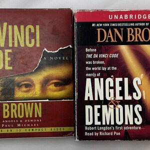 May include: Two paperback books by Dan Brown, "The Da Vinci Code" and "Angels & Demons". Both books are unabridged and feature the author's name and the title of the book in large, bold font.