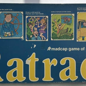 May include: The Ratrace board game box, featuring a blue background with yellow text and illustrations. The box includes the game's title, "Ratrace," and the tagline, "A madcap game of social climbing."