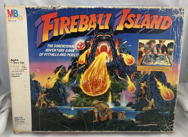 May include: Vintage Fireball Island board game box. The box features a vibrant illustration of a volcanic island with a fiery eruption. The game is for 2 to 4 players, ages 7 and up. The box has the Milton Bradley Company logo.