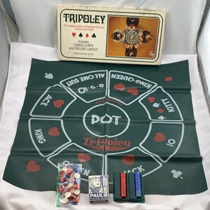 May include: A vintage Tripoley game set. The set includes a green game board with card suit symbols, a box, chips, and a deck of Paulson playing cards. The box reads "Tripoley" and "The original game of Michigan Rummy Hearts and Poker."