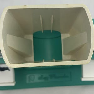 May include: An overhead view of a seed planter. The planter is primarily green and off-white, with a large, open hopper and two transparent seed compartments on either side. The base has the text "Slogg Products".