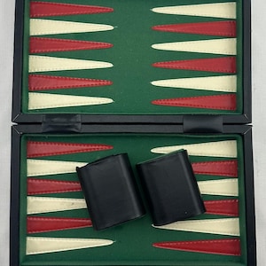 May include: Open backgammon board with a green playing surface, red and white triangles, and black leather dice cups. Includes dice and game pieces. The board is in a black case.