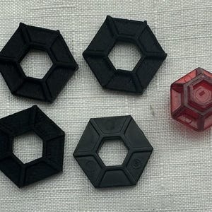May include: An assortment of black and red hexagonal objects. Four black objects have a hollow center, while the red object is translucent. The objects are arranged on a textured, light gray surface.